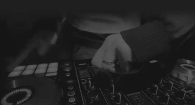Dłoń DJ-a manipulująca pokrętłami na konsoli do miksowania muzyki.