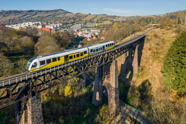 Żółty pociąg Kolei Dolnośląskich jedzie po wiadukcie nad miastem, idealny sposób, gdzie w góry pociągiem.