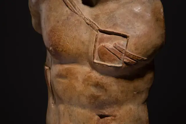 Fragment rzeźby przedstawiający tors mężczyzny z wyciętym prostokątem na klatce piersiowej.