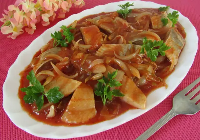 Pyszne śledzie po cygańsku w sosie pomidorowym z cebulką, udekorowane natką pietruszki.
