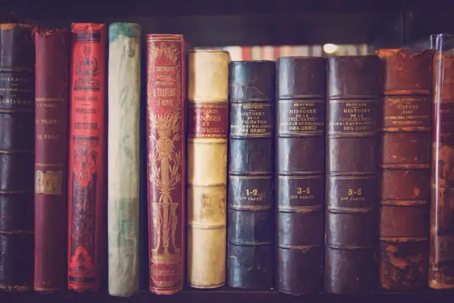 Rząd starych, oprawionych w skórę książek na półce.