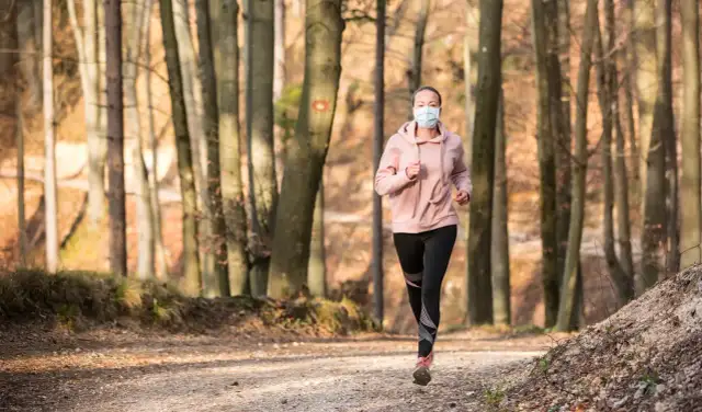 Femme courant en forêt avec un masque de protection.