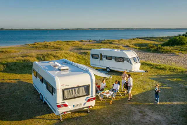 Rodzina odpoczywa przy przyczepach kempingowych nad morzem.