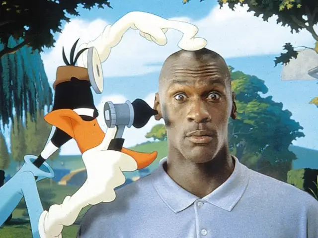 Michael Jordan z zaskoczoną miną, gdy Kaczor Daffy próbuje mu coś włożyć do ucha. Zabawna scena z komedii dla dzieci.
