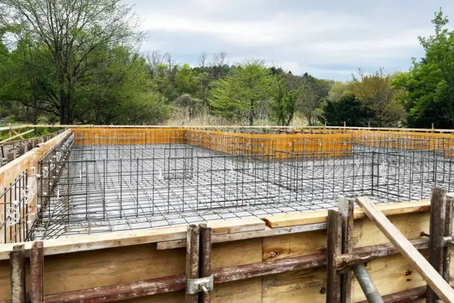 Siatka zbrojeniowa w drewnianej formie fundamentowej na tle zieleni.