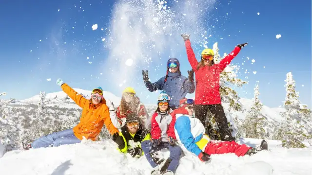 Grupa narciarzy w kolorowych strojach rzuca śniegiem na tle ośnieżonych gór.