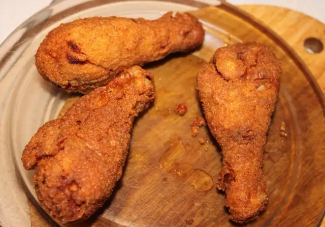 Trzy złociste, chrupiące pałki kurczaka na drewnianej desce.