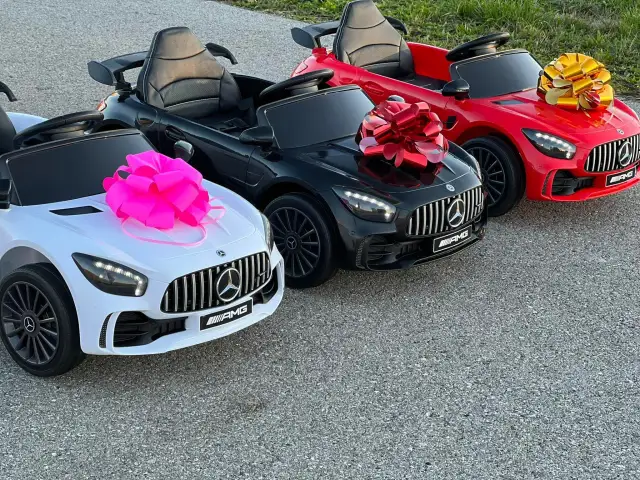 Trzy jeżdżące samochody dla dzieci w kolorach białym, czarnym i czerwonym, ozdobione kokardami.
