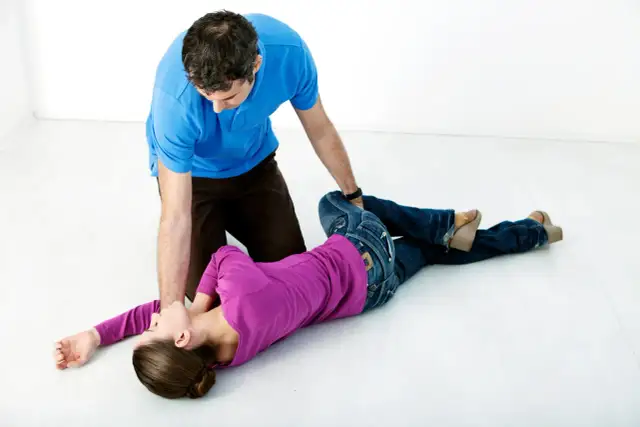 Mężczyzna w niebieskiej koszulce klęczy obok kobiety leżącej na boku w fioletowej bluzce i dżinsach.