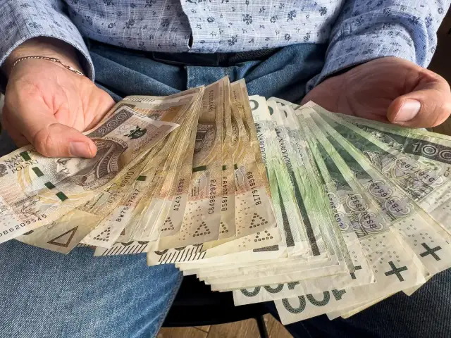 Dłonie trzymające plik polskich banknotów. Czy od pożyczki płaci się podatek? Pieniądze mogą być odpowiedzią.