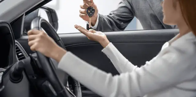 Kluczyki do nowego auta przekazuje sprzedawca, a klientka zastanawia się: leasing czy gotówka?
