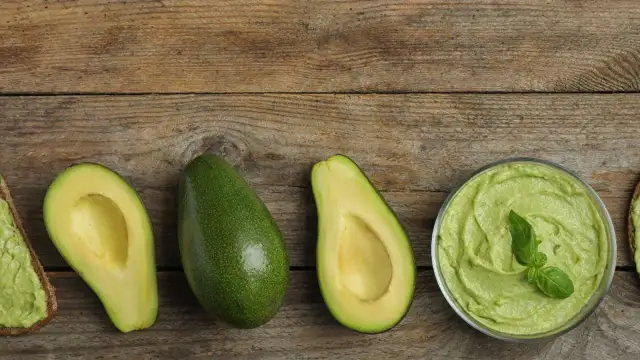 Angeschnittene und ganze Avocados sowie Avocadocreme auf Holzuntergrund.