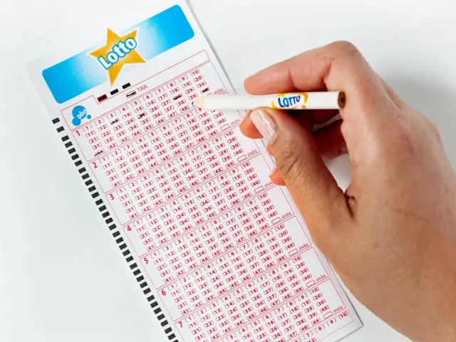Dłoń z ołówkiem Lotto zaznacza liczby na kuponie. Czy czwórka w Lotto Plus przyniesie szczęście?