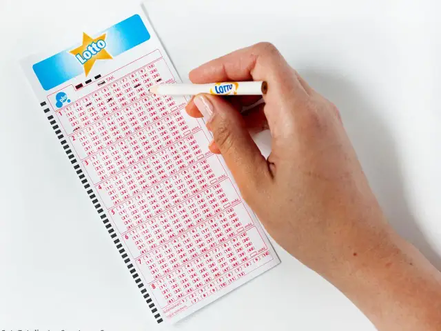 Dłoń z ołówkiem zaznacza liczby na kuponie Lotto. Zastanawiasz się, lotto ile jest do wygrania?