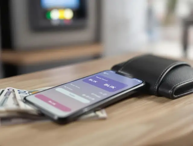 Smartfon z aplikacją BLIK, obok portfel i banknoty na drewnianym stole.