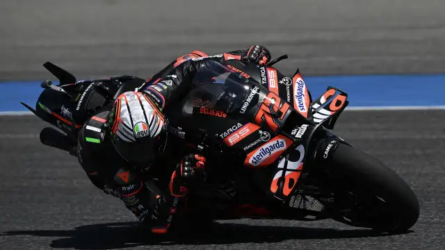 Motociclista de MotoGP inclinado en una curva, con su moto negra y naranja.