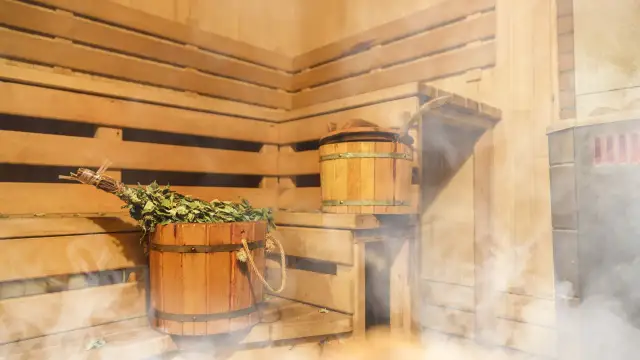 Drewniana sauna z miotełką i wiadrem, idealna na relaks po treningu. Para unosi się, tworząc przytulną atmosferę.