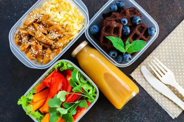 Zdrowe przepisy na lunch do pracy: kurczak z ryżem, sałatka z warzywami, czekoladowe wafle z jagodami i sok.