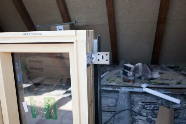 Drewniane okno Fakro z uchwytem montażowym, gotowe do instalacji z użyciem taśmy do ciepłego montażu okien. W tle widać materiały budowlane.