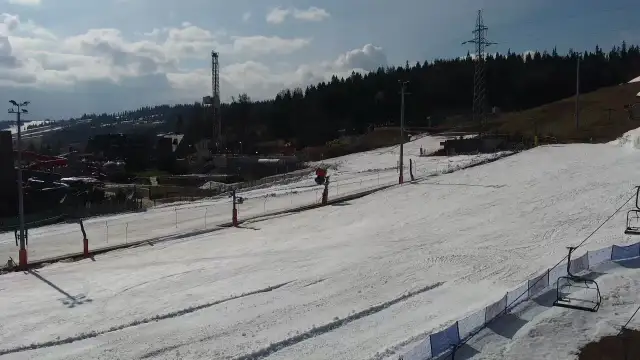 Widok z białka tatrzańska webcam na ośnieżony stok narciarski z wyciągiem krzesełkowym i wieżą w tle.