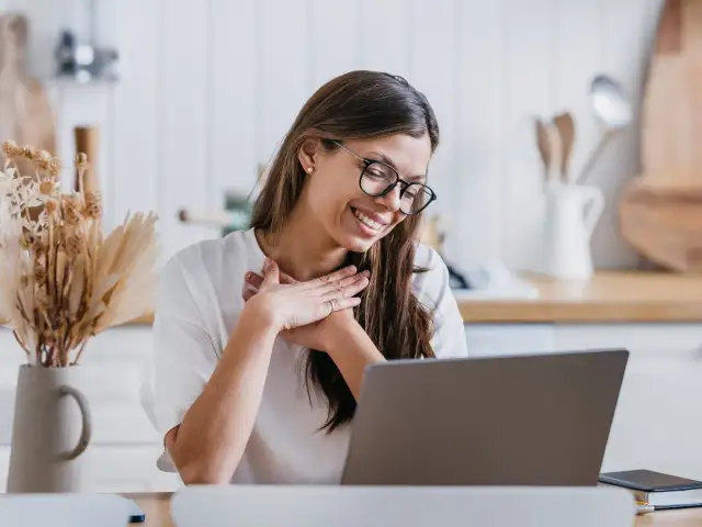 Uśmiechnięta kobieta z dłońmi na sercu, jakby czytała inspirujące cytaty o podziękowaniu.