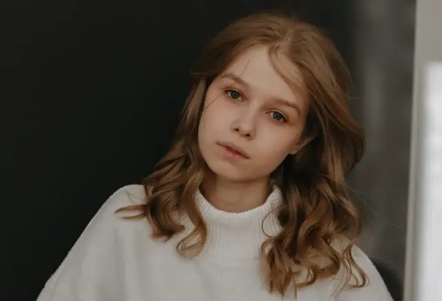 Młoda dziewczyna z burzą brązowych włosów, w białym golfie, zamyślona. Zastanawia się, jak przeprosić dziewczynę, by naprawić błąd.