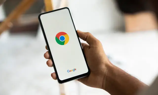 Dłoń trzyma smartfon z logo Chrome. Chcesz wiedzieć, jak usunąć synchronizację Google?