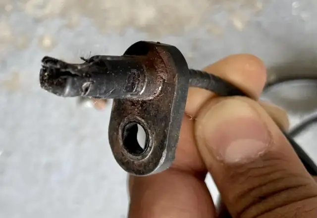 Uszkodzony czujnik ABS w tylnym kole, z widocznymi śladami zużycia i korozji. Może to powodować problemy z systemem hamulcowym.