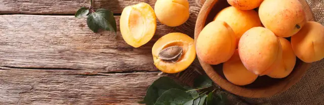 Dojrzałe morele w drewnianej misie i połówki owoców na drewnianym blacie. Zastanawiasz się, po ilu latach owocuje morela?