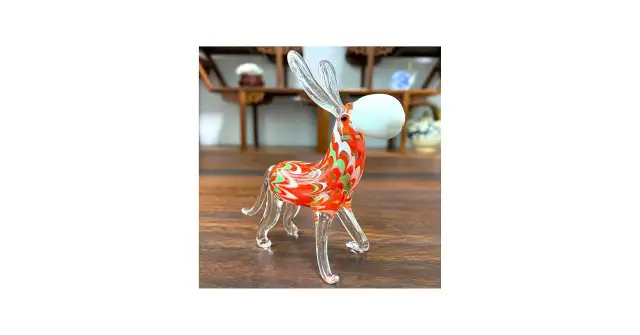 Szklana rzeźba osiołka w kolorze pomarańczowo-zielonym na drewnianym tle.