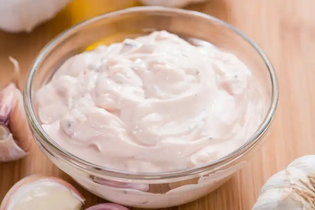 Kremowy wegański majonez z czosnkiem, przygotowany z roślinnych składników. Idealny dodatek do potraw.