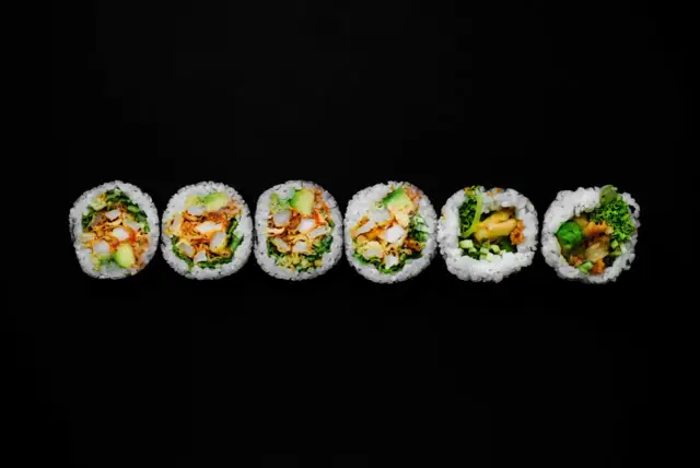Sześć kawałków futomaki z awokado, kurczakiem i warzywami na czarnym tle.