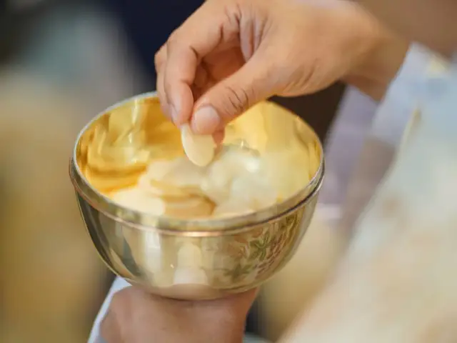 Dłoń bierze opłatek z kielicha podczas komunii świętej.