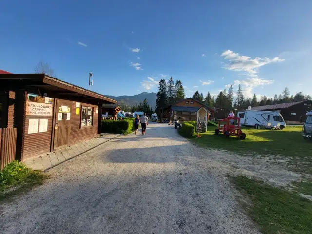Słoneczny dzień na **camping Oravice**. Drewniany budynek recepcji, przyczepy kempingowe i zielone wzgórza w tle.
