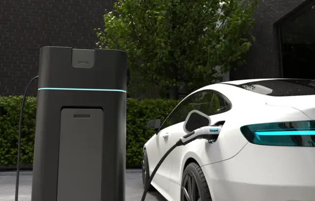 Biała Tesla ładuje się przy nowoczesnej stacji. Wyświetlacz pokazuje postęp ładowania, dając odpowiedź na pytanie, jak długo ładuje się Tesla.