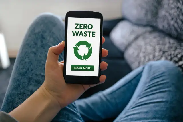 Dłoń trzyma smartfon z ekranem aplikacji zero waste. Zielony symbol recyklingu i przycisk "Learn More" zachęcają do ekologicznych działań.