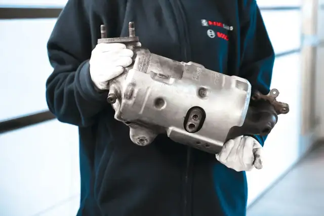 Osoba w białych rękawiczkach trzyma metalowy element filtra DPF.