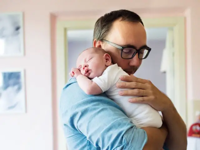 Ojciec tuli śpiące dziecko na ramieniu, stosując jedną z najlepszych pozycji do odbijania.