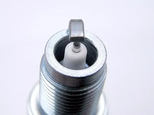 Zbliżenie na końcówkę świecy zapłonowej z białym izolatorem i metalową elektrodą.