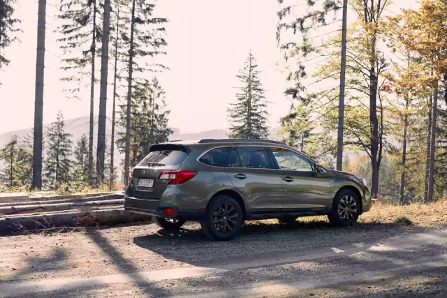 Zielone auto z napędem 4x4 zaparkowane na leśnej drodze wśród drzew.