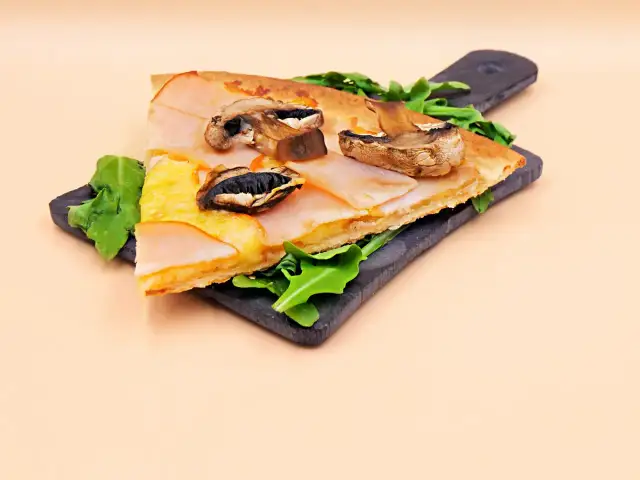 Kawałek pizzy capriciosa z szynką, serem i pieczarkami na ciemnej desce.