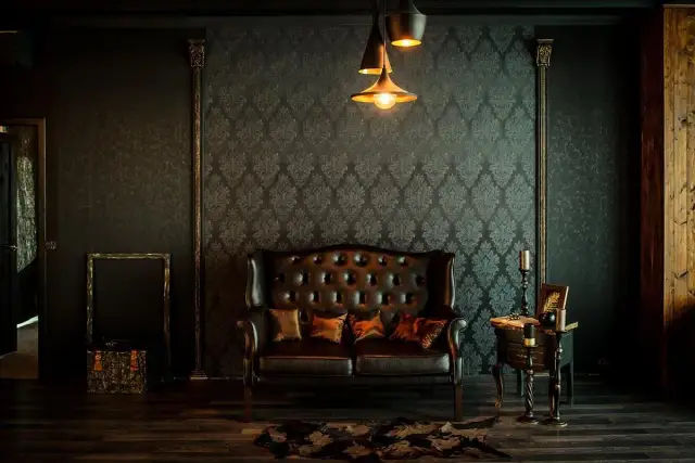 Elegancka skórzana kanapa i stolik tworzą przytulny kącik. Wnętrze w stylu vintage, z tapetą w ornamenty i stylowymi lampami, zaprasza do relaksu.