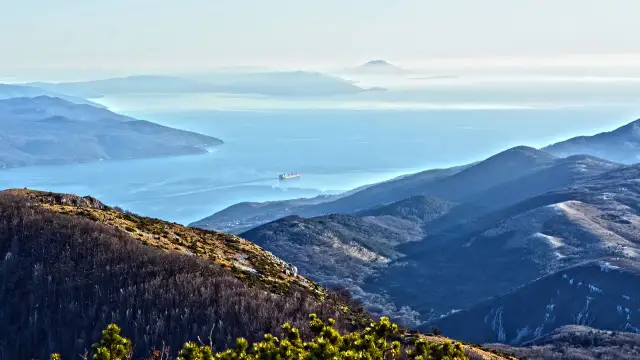 Widok z Učka Nature Park na zatokę z kontenerowcem. Góry w odcieniach niebieskiego i zieleni.