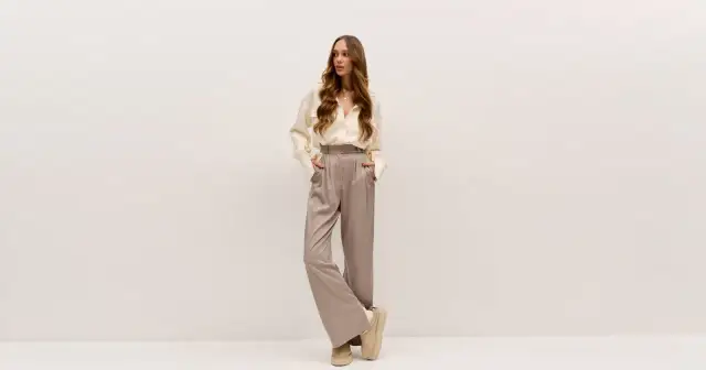 Młoda kobieta w eleganckim, beżowym zestawie: luźna koszula i szerokie spodnie.
