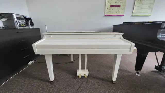 Biały fortepian z złotymi detalami i czarny fortepian w tle.