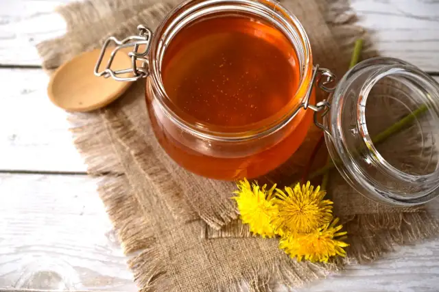 Słoik pełen złotego syropu z mniszka, obok świeże kwiaty.