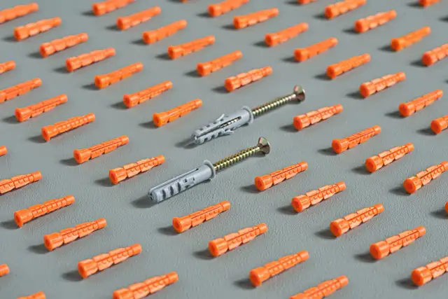 Pomarańczowe kołki rozporowe i dwa kołki z wkrętami na szarym tle.