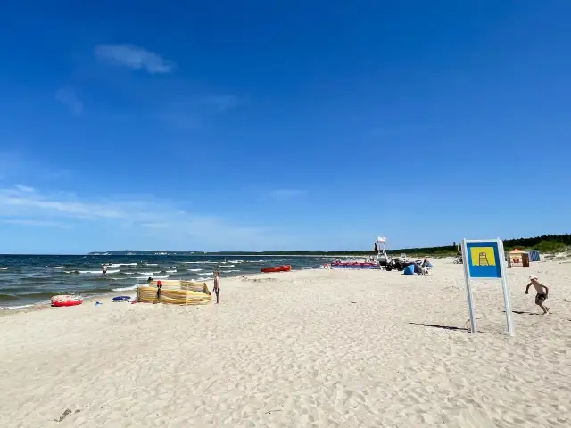 Słoneczna plaża Cztery Wiatry z piaskiem, morzem i ludźmi. W oddali widać ratownika na wieży.