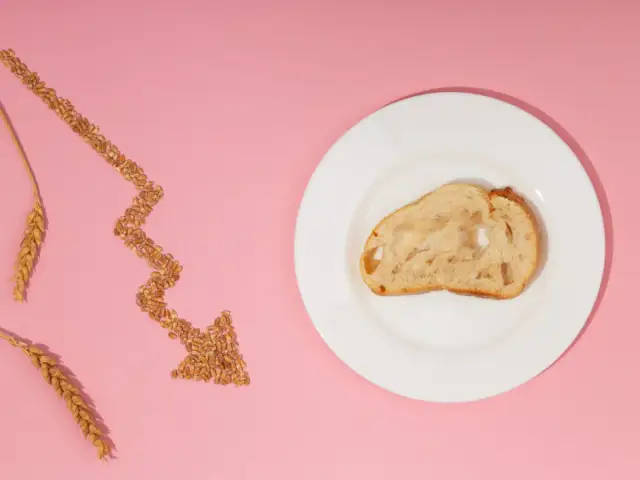 Strzałka z ziaren pszenicy i kromka chleba na talerzu na różowym tle.