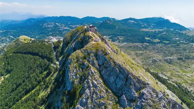 Majestatyczne czarnogóra góry z budynkiem na szczycie, otoczone zielonymi lasami i skalistymi zboczami.